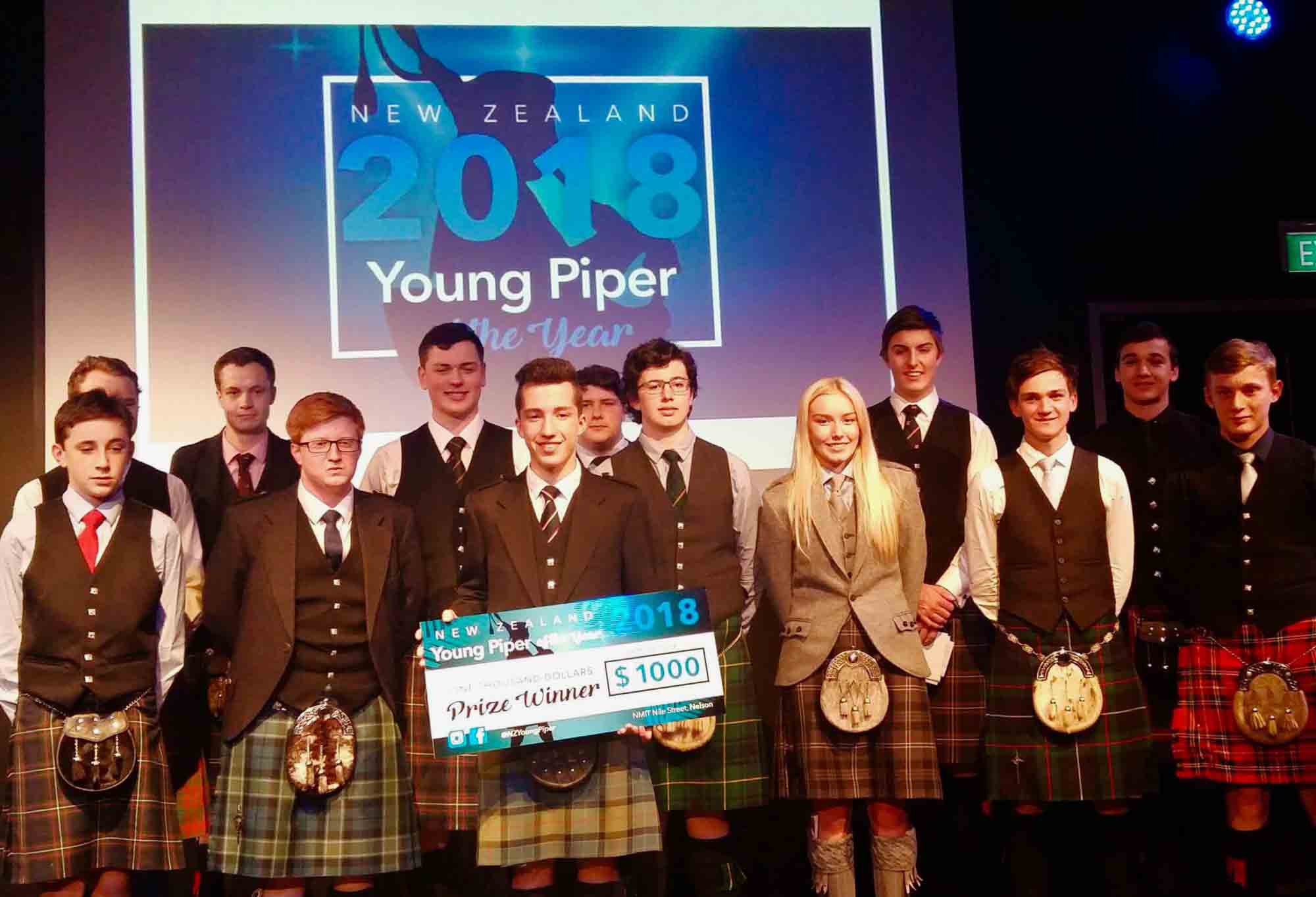 Campbell Wilson holds his presentation cheque for winning the 2018 NZ Young Piper of the Year competition, with other prize-winners looking on.