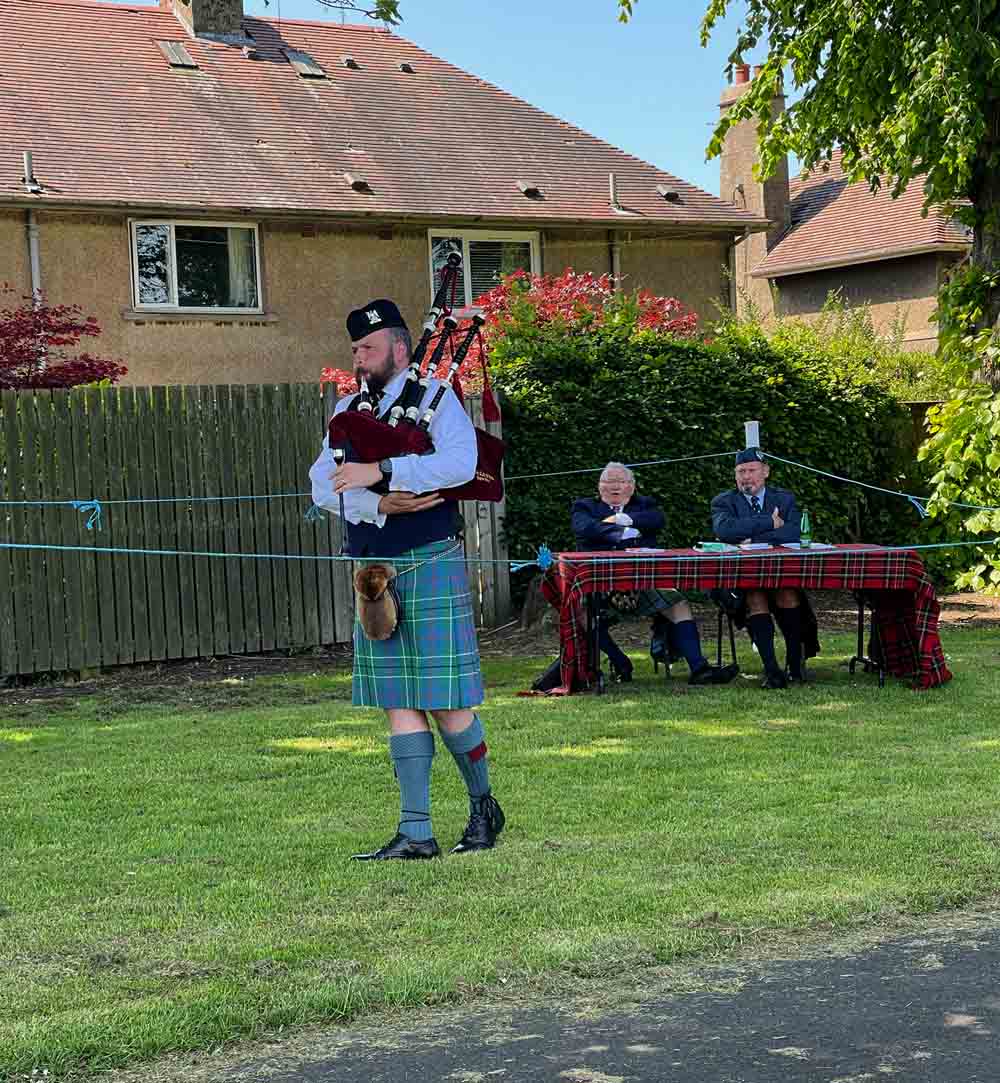 Ben Duncan flattening the grass in the MSR at Markinch Games before judges Jimmy Banks and Roderick Barron.