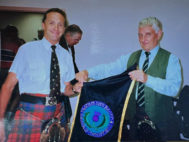 Ian Whitelaw (left) being presented with the Banner of the Mountains (Bratach nam Beann) for piobaireachd at the annual Couer d'Alene, Idaho, summer school by Andrew Wright.