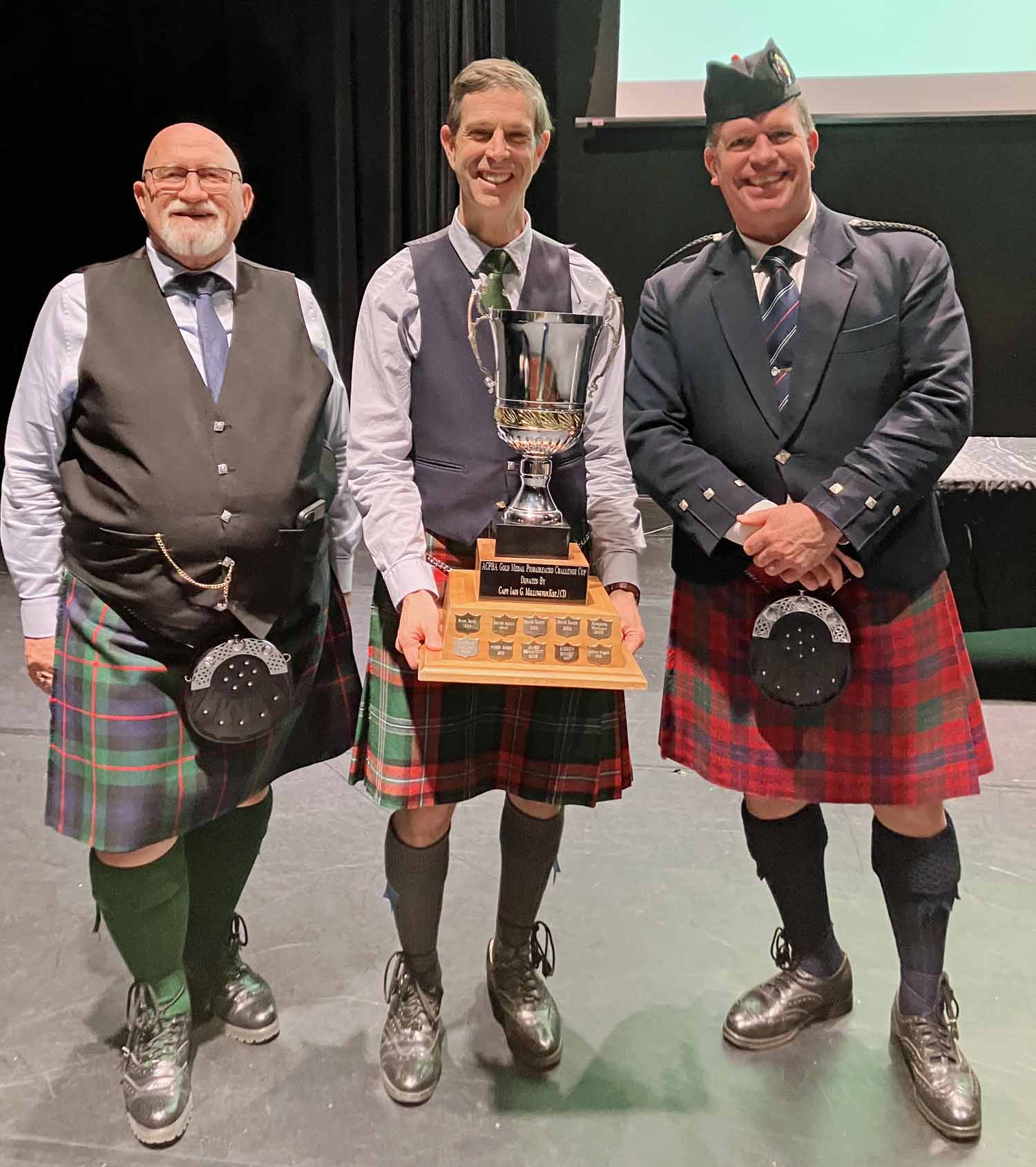 James MacHattie (centre) accepts the Piobaireachd trophy at the 2025 Atlantic Canada Piobaireachd Challenge from ACPBA Chief Steward Gordon Murray (left) and judge Ian K. MacDonald.