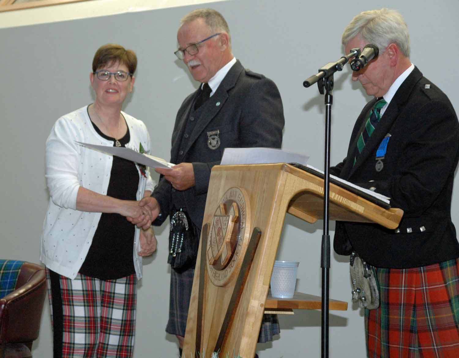 Leanne Bradshaw receiving Hall of Fame induction certificate from Robert Cochrane, President of the Antigonish Highland Society, as Iain Boyd reads the citation.